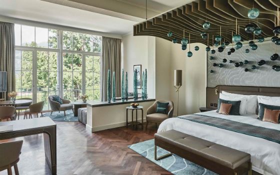 Moderne Hotelsuite mit Designelementen und Gartenblick durch bodentiefe Fenster. 