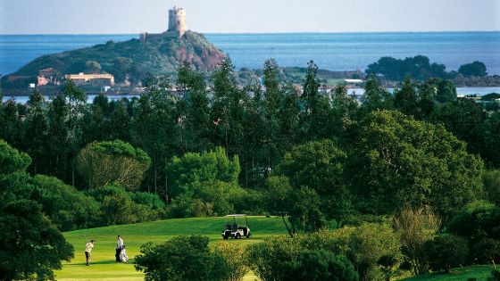 Personen auf einem Golfplatz, umgeben von Wald, an einer Küste mit vorgelagerter Insel mit Turm. 