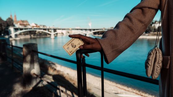Eine Person vor dem Stadtpanorama von Zürich am Fluss stützt sich auf den Griff eines Trolleys und hat dabei eine goldene Kreditkarte in der Hand.