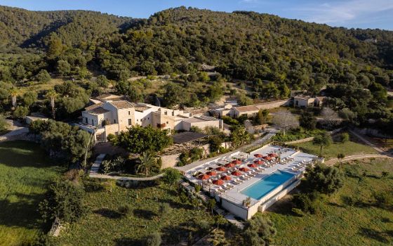 In einer Berglandschaft ist ein beiges Gebäude mit Pool und Liegen umgeben von der Natur. 