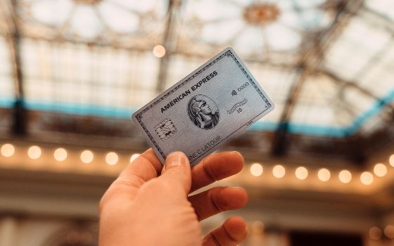 Eine Hand hält eine silberne Platinum Kreditkarte von American Express hoch in einem Gebäude mit Jugendstil-Glasdecke.