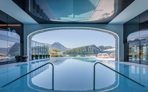 In einem Hotel-Spa liegt ein Infinity-Pool direkt am See mit Blick auf die Berge.