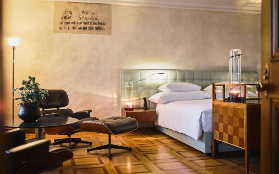 Stilvolles Hotelzimmer mit Doppelbett und Ledersessel auf Parkettboden. 
