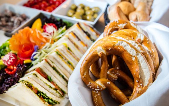 Verschiedene Teller, Schüsselchen, ein Korb mit Brezeln, Sandwiches, Salat und weiteren Snacks.