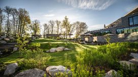 Ein Hotel steht in einer grünen Hügellandschaft, umgeben von Bäumen und dekorativen Steinen.