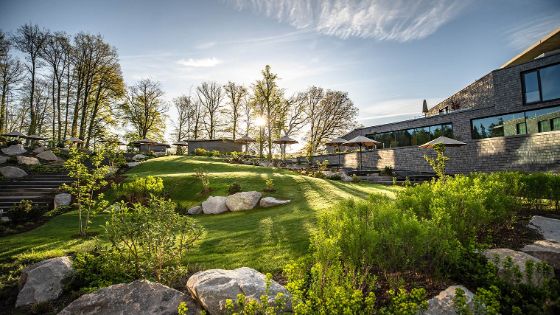 Ein Hotel steht in einer grünen Hügellandschaft, umgeben von Bäumen und dekorativen Steinen.