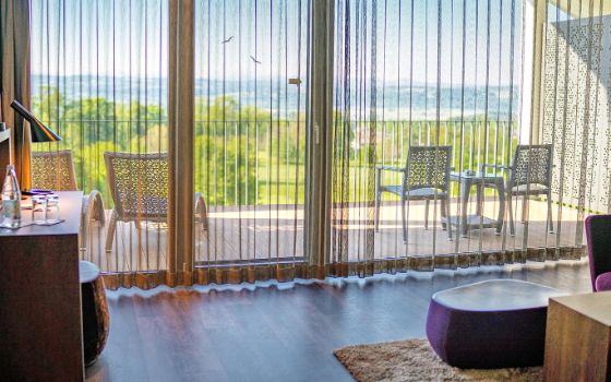 In einem Hotelzimmer ist ein bodentiefes Fenster, das zu einem grossen Balkon führt.