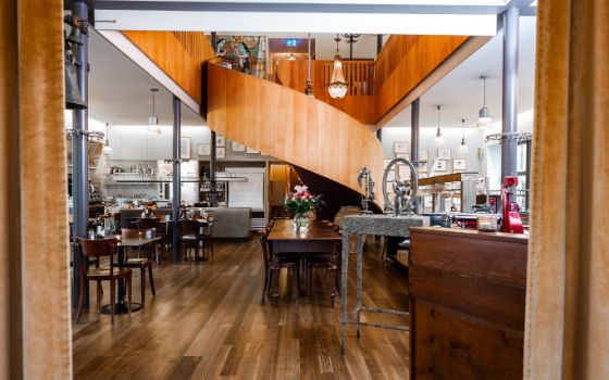 Gastraum eines Restaurants mit Holztischen und -stühlen, in dem eine Wendeltreppe aus Holz nach oben führt.