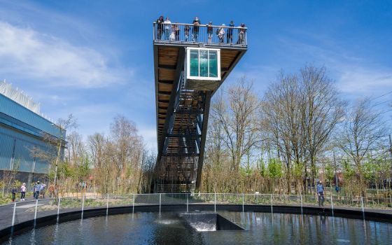 Mehrere Personen stehen auf einer Plattform mit quadratischem Wassertank über einem Wasserbecken in einer Aussenanlage.