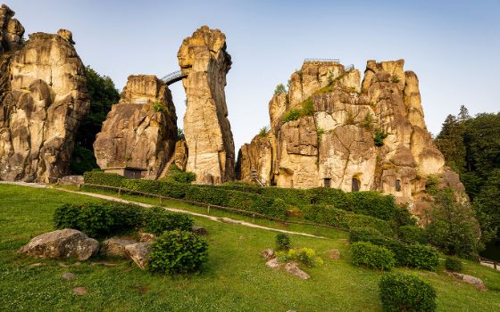 Ensemble markanter Felsformationen hinter einer gepflegten Grünfläche unter blauem Himmel. 