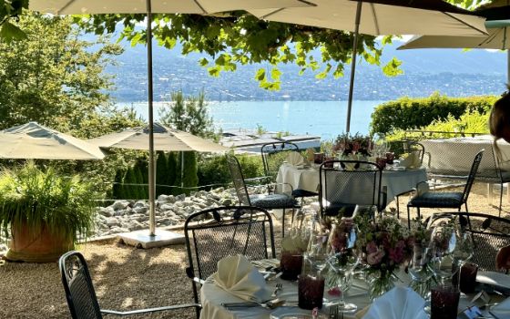 Ein von Sonnenschirmen überdachter begrünter Schottergarten mit arrangierten und gedeckten runden Tischen und Metallstühlen, im Hintergrund der Zürichsee.