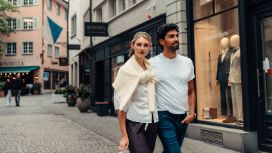 Ein junges Paar spaziert in einer Einkaufsstrasse mit Geschäften.