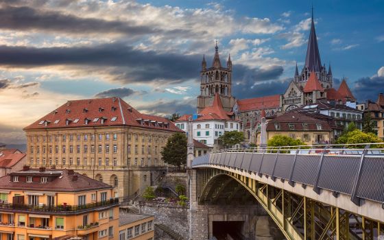 Blick auf die Kathedrale von Lausanne mit umliegenden Häusern und der modernen Brücke über die Metro-Linie bei Abendstimmung.