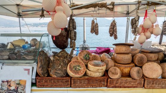 Ein überdachter Marktstand mit Käse- und Wurstwaren an einem See. 