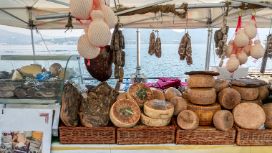 Ein überdachter Marktstand mit Käse- und Wurstwaren an einem See. 