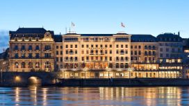 Blick am Abend auf ein grosses, historisches Gebäude mit Beleuchtung, im Vordergrund Wasser.