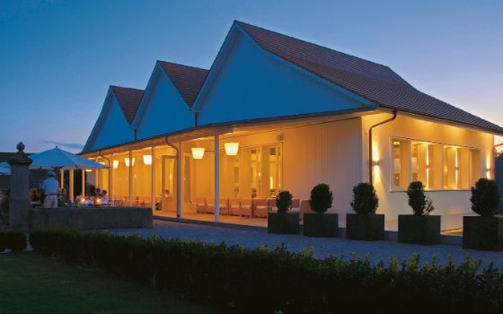 Auf einem Golfplatz steht ein weisses Restaurant, das beleuchtet ist. 