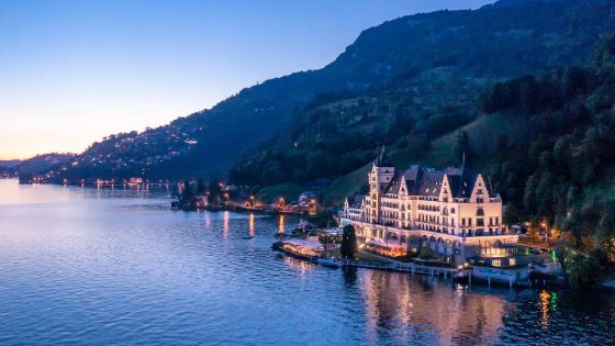 An einem grossen See steht ein kleines Schloss vor einer Bergkulisse. 