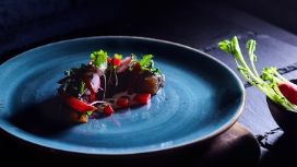 Auf einem blauen Teller ist ein kleines Gericht mit geräuchertem Lachs angerichtet.
