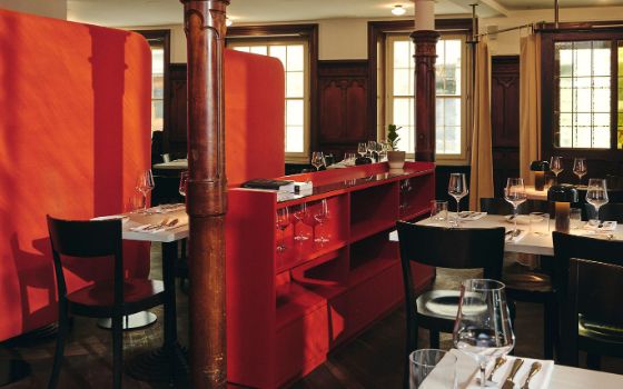 In einem Restaurant mit dunklen Möbeln steht in der Mitte ein rotes Sideboard, an der linken Wand befindet sich eine rote Stoffwand.