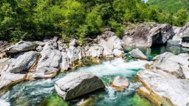 In einer steinigen Landschaft fliesst ein Fluss um einen grossen Felsen.