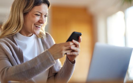 Blonde Frau blickt lachend auf ihr Smartphone.