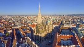 Luftaufnahme der Stadt Wien mit Stephansdom und seinem bunten Dach im Fokus, rundherum Häuserblöcke. 