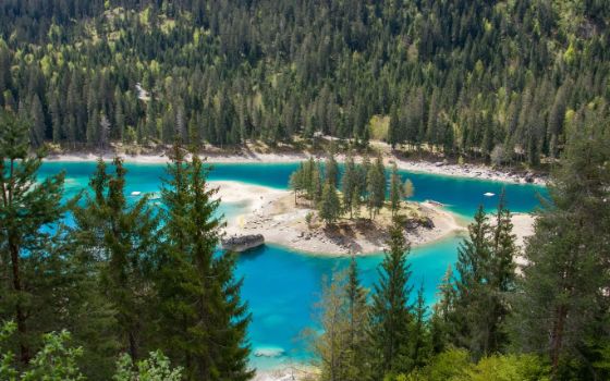 Blick auf den türkisblauen Caumasee mit Waldinsel und umgebenden Nadelbäumen