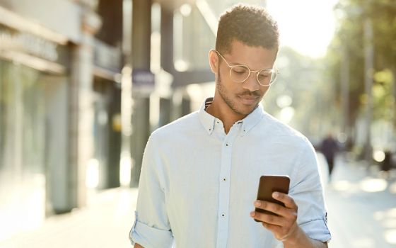 Ein junger Mann läuft auf der Strasse und schaut dabei auf sein Smartphone.