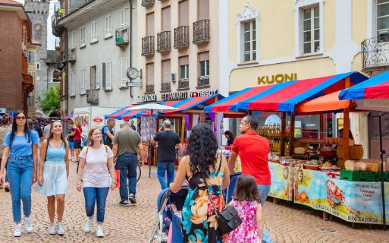 Personen spazieren durch eine Strasse, an den Seiten sind bunte Stände aufgebaut. 