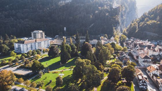 Hotelkomplex mit Parkanlage an einer Kleinstadt am Fusse eines bewaldeten Berges. 