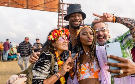 Vier Personen mit bunter Kleidung, Brillen und Blumenschmuck machen ein Selfie. 