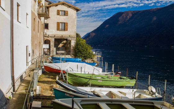 Boote am Ufer des Lago di Lugano im Fischerdorf Gandria mit historischen Häusern und Blick auf die umliegenden Berge.