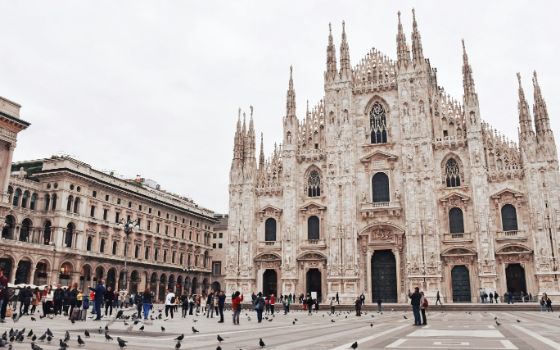 Der Mailänder Dom auf dem Piazza del Duomo mit Menschen und Tauben im Vordergrund an einem bewölkten Tag.
