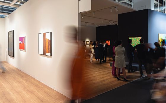 Personen in zwei Ausstellungsräumen mit modernen Gemälden in einer Halle. 