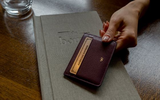 Eine Person legt ein kleines Portemonnaie, in dem eine goldene Kreditkarte von American Express steckt, auf eine Speisekarte in einem Restaurant.
