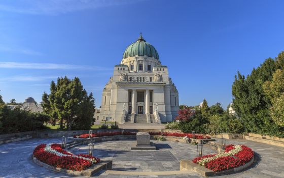 Aussenaufnahme eines Kirchengebäudes mit Kuppel auf dem Zentralfriedhof in Wien, davor geschmückte Blumenbeete. 
