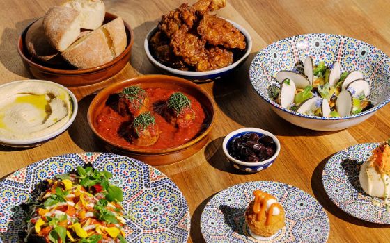 Verschiedene Gerichte stehen in kleinen bunten Schalen auf einem Holztisch, darunter, Salat, Brot und Humus.