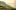 Eine Landschaft zeigt Hügel, auf denen Weinpflanzen angebaut sind, im Hintergrund liegt ein See, im Nebel scheint eine Berglandschaft. 