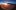 Blick auf die Tragfläche eines Flugzeugs durch ein rundes Flugzeugfenster bei Sonnenuntergang über den Wolken