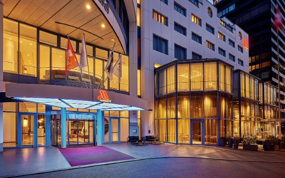 Moderne, beleuchtete Aussenfassade mit Eingangsbereich zu einem Hotel mit Marriott Logo bei Dunkelheit.