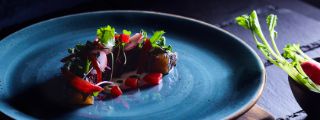 Auf einem blauen Teller ist ein kleines Gericht mit geräuchertem Lachs angerichtet.