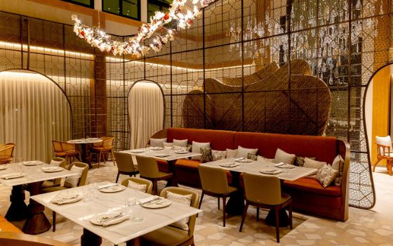 In einem Restaurant stehen Sofas und Stühle um gedeckte Tische, von der Decke hängen spektakuläre Kunstwerke aus Glas. 