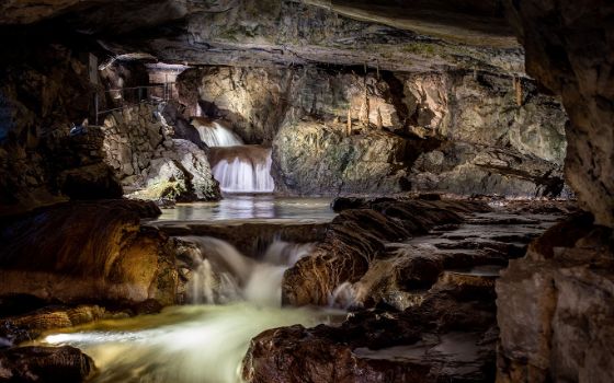 In einer Tropfsteinhöhle fliesst in der Mitte ein Wasserfall. 