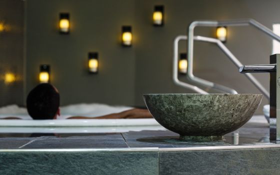 Eine Person in einem Whirlpool, im Vordergrund eine Steinschale am Beckenrand.