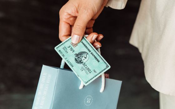 Eine grüne American Express Kreditkarte zusammen mit einer kleinen Papiertragetasche, gehalten von einer weiblichen Hand