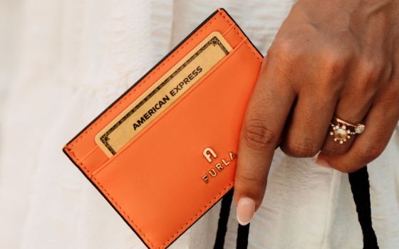 Nahaufnahme einer goldenen American Express Kreditkarte in einem orangefarbenen Lederetui in einer weiblichen Hand