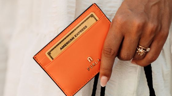 Nahaufnahme einer goldenen American Express Kreditkarte in einem orangefarbenen Lederetui in einer weiblichen Hand