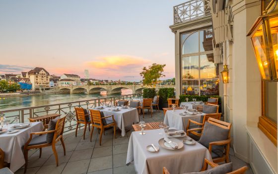 Die stilvoll eingerichtete Terrasse im Restaurant Cheval Blanc mit Blick auf den Rhein in der Stadt Basel. 