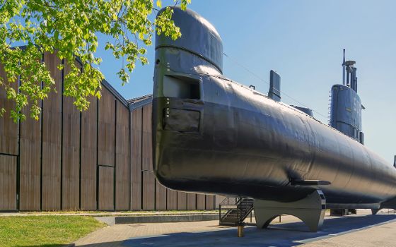 Ein grosses Uboot steht auf einem Platz, im Hintergrund befinden sich Holzhäuser. 